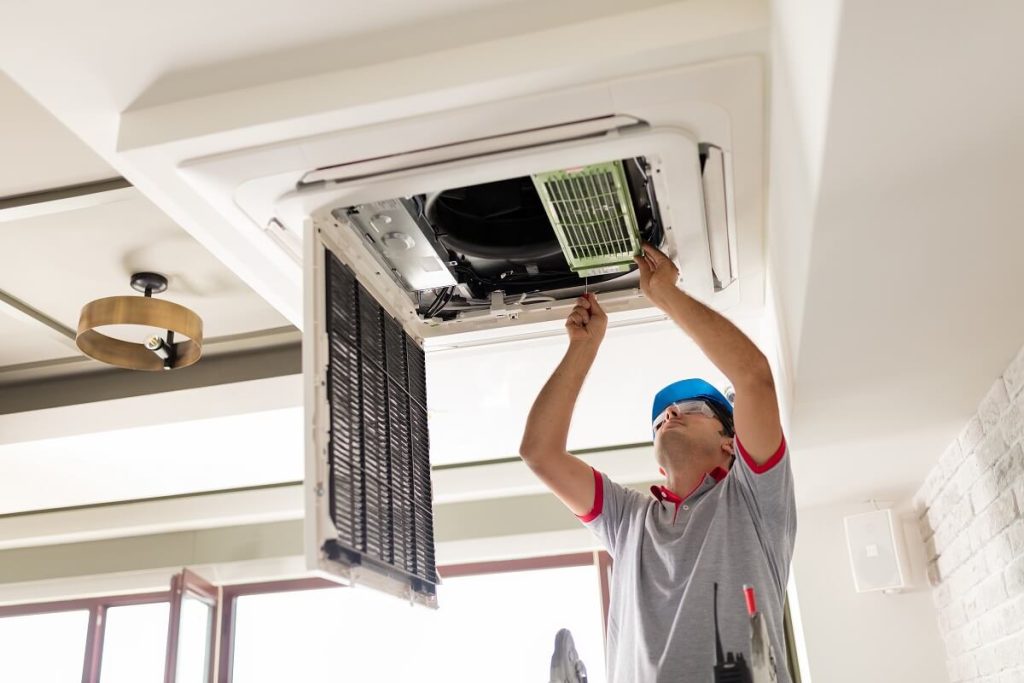 technician servicing a ducted heating unit in a ceiling cavity, showing filters and burner components being checked