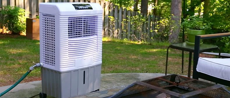 A mobile evaporative cooler on wheels on a sunny patio or deck by the ocean, illustrating how it can be moved around easily.
